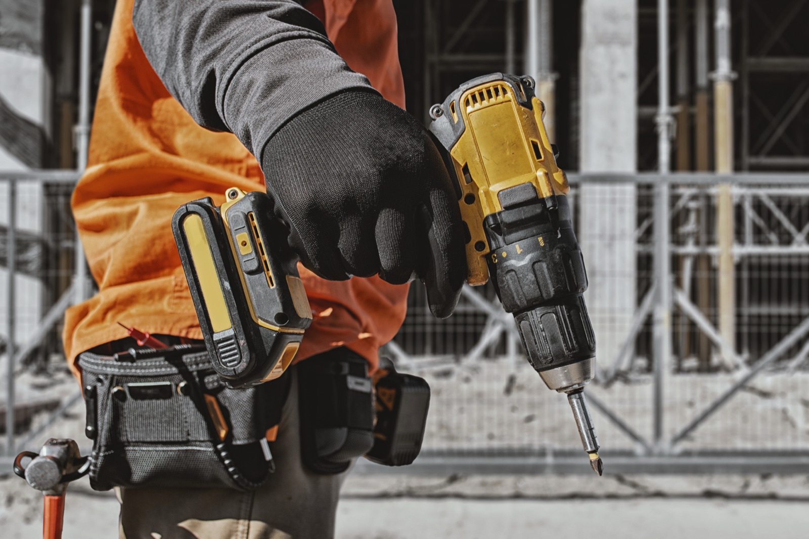 Gloved worker holding a cordless drill/driver with a screwdriver bit in the chuck on a construction site