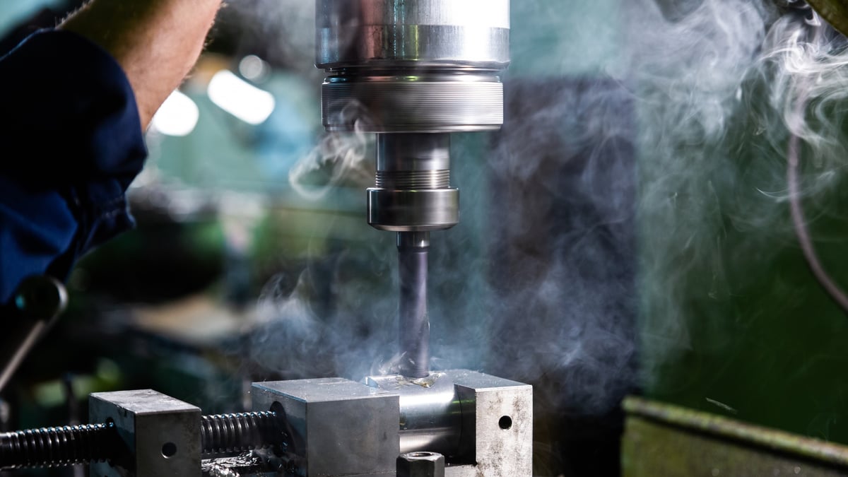 Drill press cutting into steel with smoke rising from the hot bit