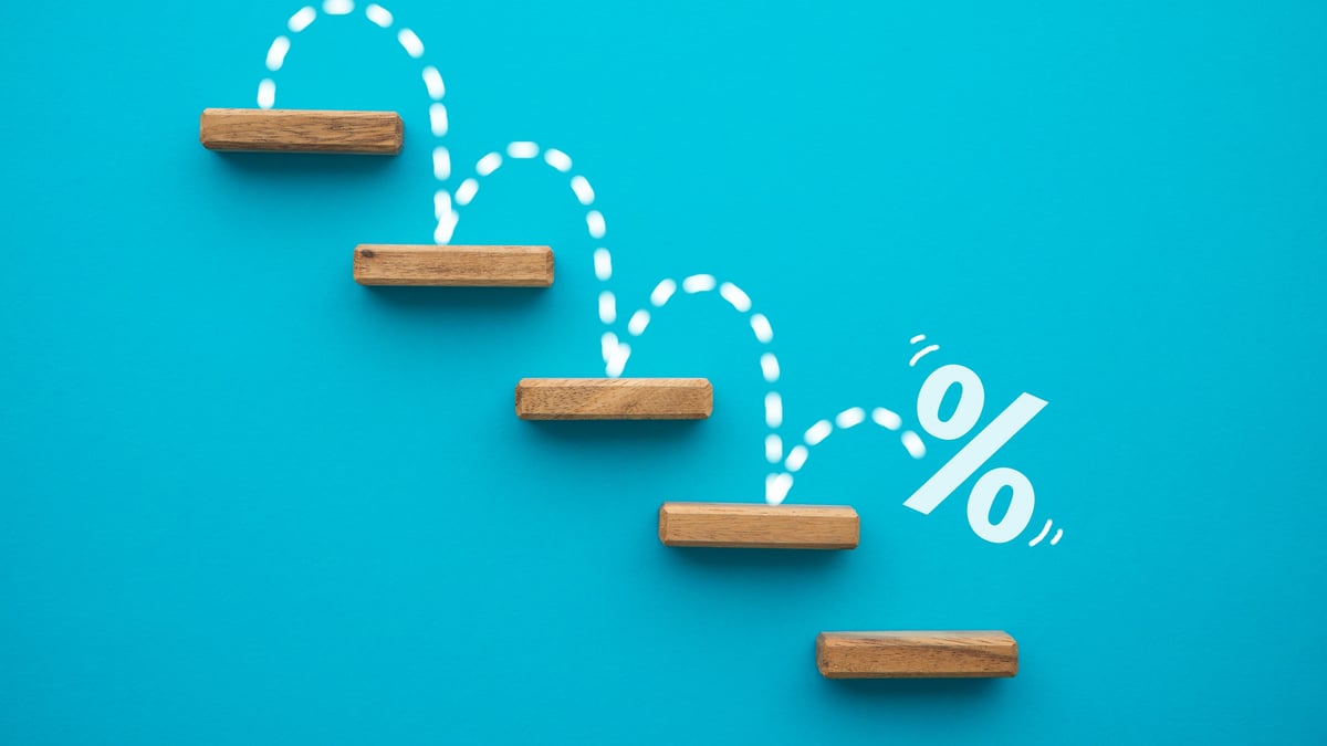 Percent sign stepping down a staircase of wooden blocks on a blue background