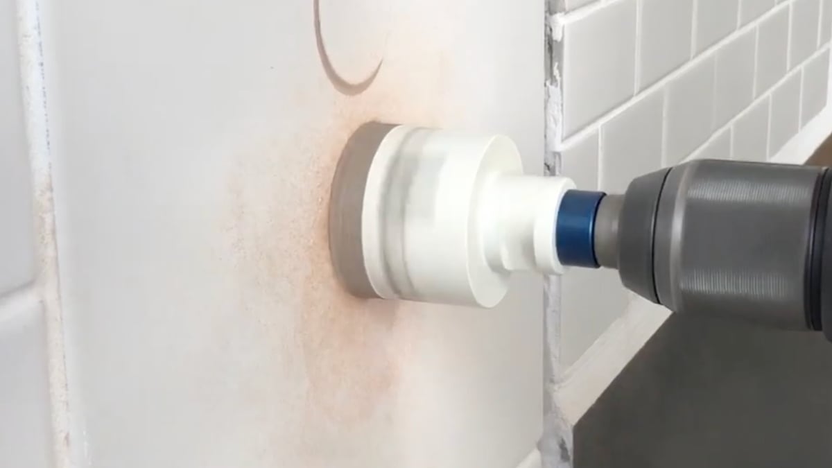Diamond hole saw drilling a large hole through a white wall beside subway tile