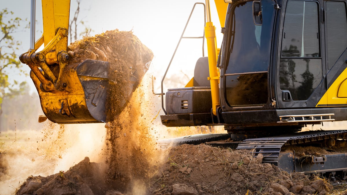 Excavator dumping a bucket of soil on a construction site at sunset