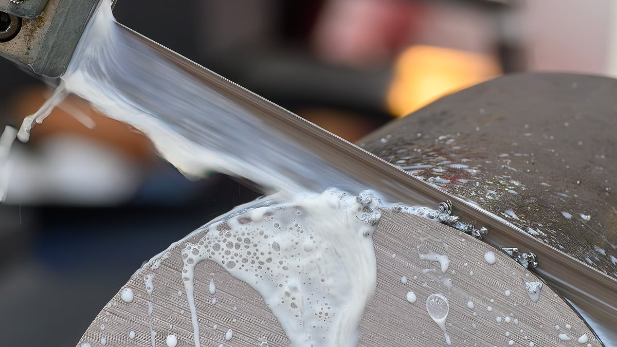 Band saw blade cutting a solid steel bar with coolant spraying off the cut