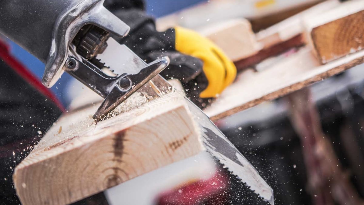 Reciprocating saw cutting through a wood beam, sawdust flying