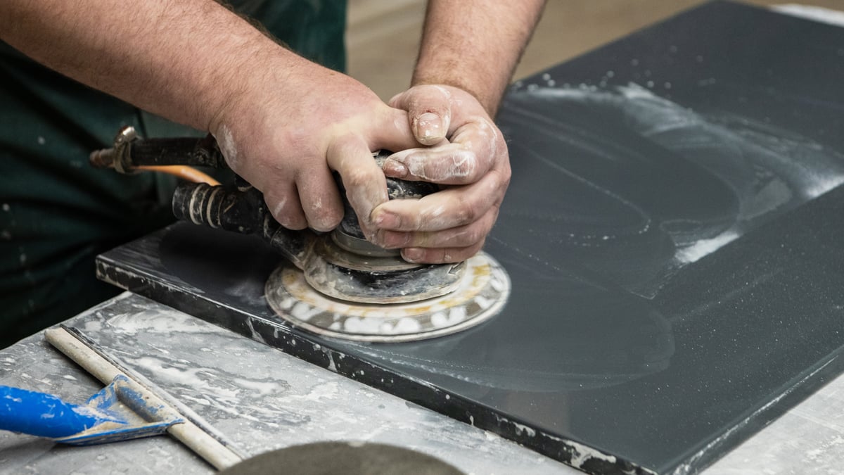 Fabricator polishing the edge of a dark stone countertop slab in a fabrication shop