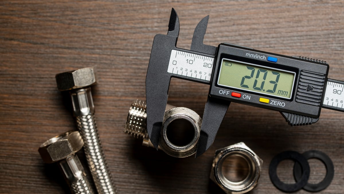 Digital caliper measuring a threaded pipe fitting on a wood bench